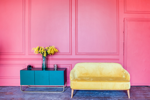 Pink wall, yellow sofa and blue bedside table with flowers.
