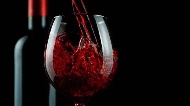 Detail of pouring red wine into glass, isolated on black background. Free space for text