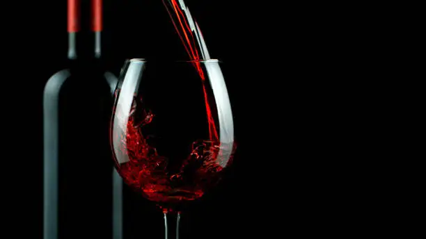 Detail of pouring red wine into glass, isolated on black background. Free space for text