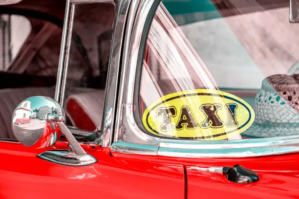 Historic american car in Havana with taxi sticker on windshield and straw hat lying on the dashboard