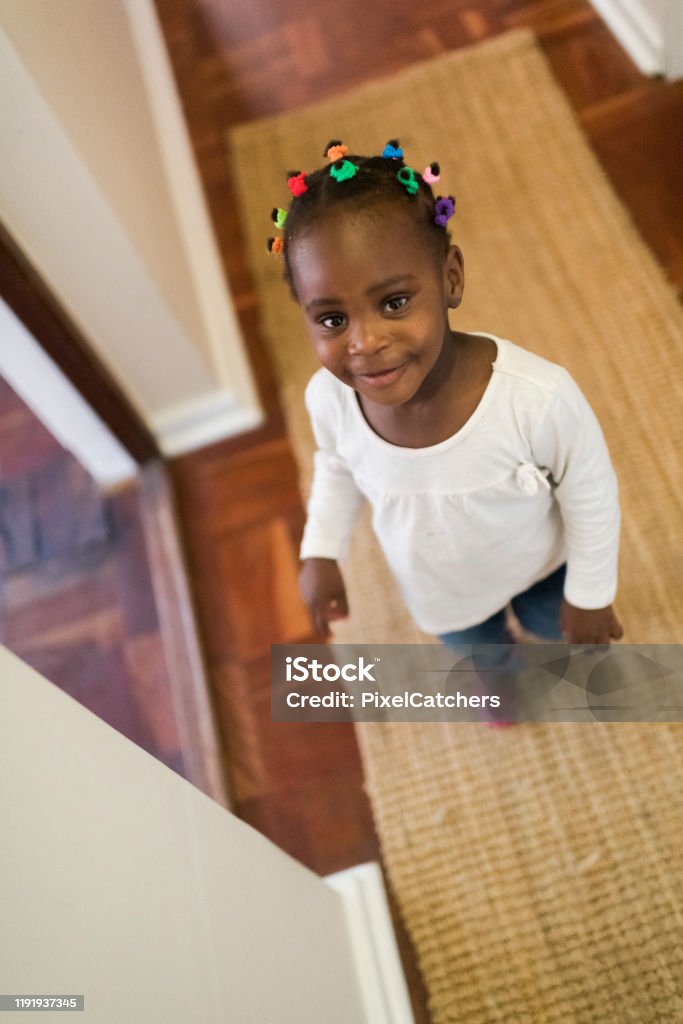 High angle view of a cute smiling 2year old girl looking at the camera High angle view of a cute smiling girl looking at the camera, standing in passage way at home. 2-3 Years Stock Photo