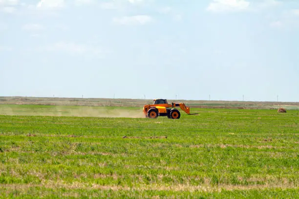 An agricultural tractor loader loads bales of hay into a tractor trailer on the field