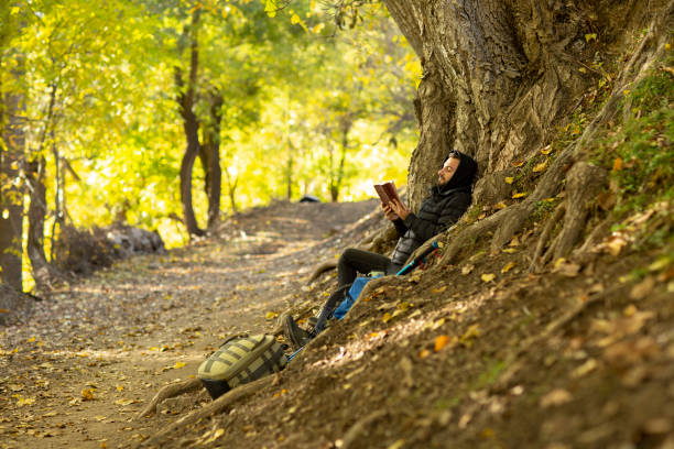 A man reads in the autumn forest sitting on a tree.