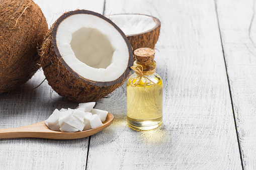Glass bottle of coconut oil with fresh coconut fruit on wooden rustic background, alternative theraphy medicine concept, Cocos nucifera