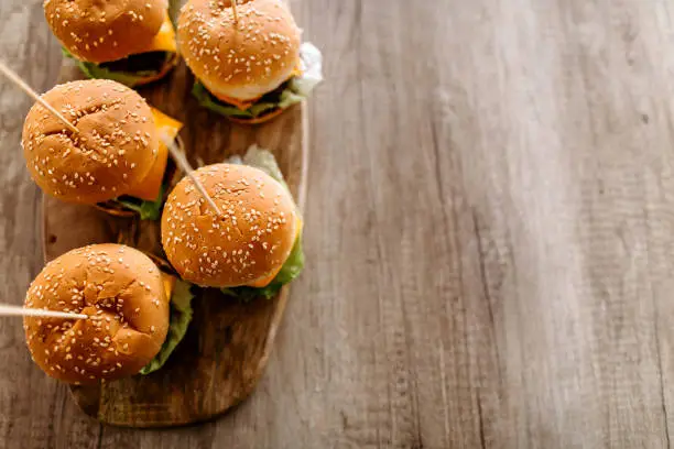 Close up of homemade cheeseburgers on wooden tray served on dining table, directly above