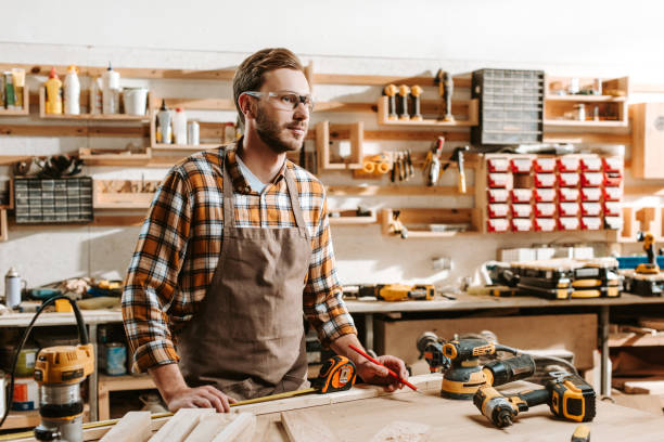 istock handsome carpenter in goggles standing near table and equipment 1191966485