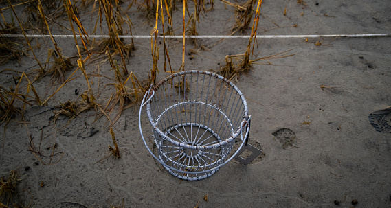 A wire basket with a measuring tool and boot tracks in the sand.