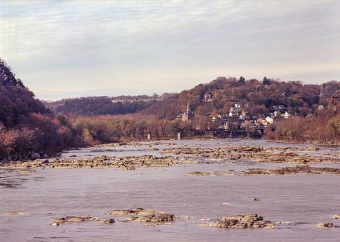 A wide shallow river with rocks strewn about and a town with a church steeple in the background.
