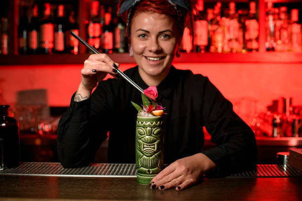 istock Smiling bartender girl serving alcoholic cocktail in the Tiki mug adding arose bud with tweezers 1191971171