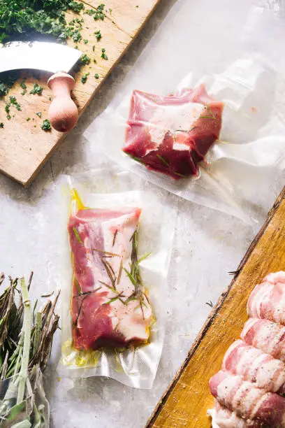 Photo of Raw roastbeef meat  prepared, caparisoned with pig caul fat and rosemary inside a sous vide bag ready to be cooked with a rooner , top view  over a brown background