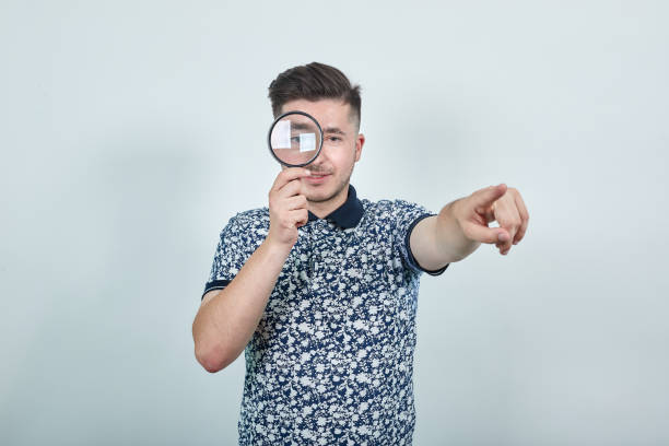 istock Young man holding a magnifying glass, looking on it, pointing directly 1191974671