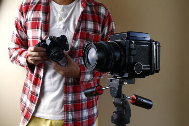 istock Man holding a 35mm film camera and standing behind a medium format film camera on a tripod 1191979431
