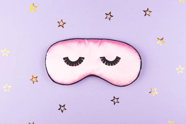 istock Cute pink sleeping mask on purple background. 1191982599