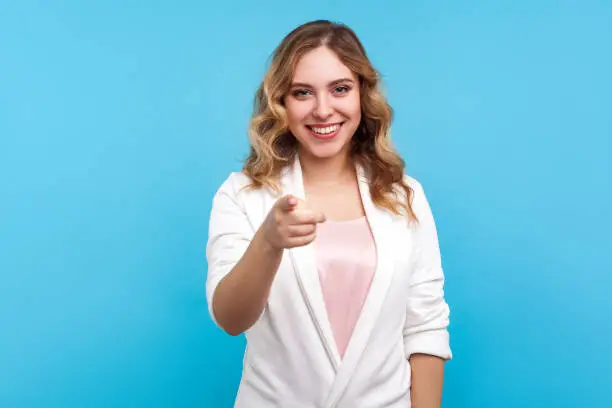 Photo of Hey you! Portrait of cheerful beautiful woman pointing finger at camera with smiling happy expression. blue background