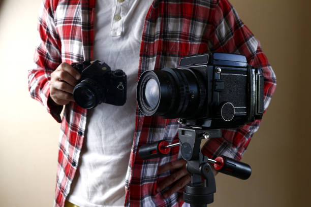 istock Man holding a 35mm film camera and standing behind a medium format film camera on a tripod 1191984071
