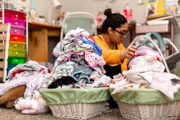 madre millennial hispana abrumada con montones de ropa de bebé - ropa de bebé fotografías e imágenes de stock