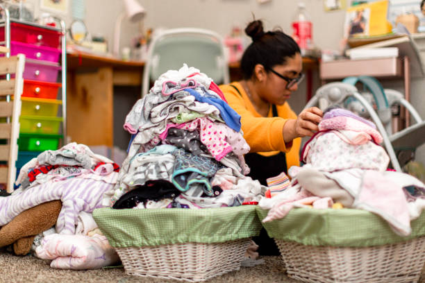 Hispanic Millennial Mother Overwhelmed With Piles of Baby Clothes First time millennial mother overwhelmed with the heaps of baby laundry to fold and organize. Two baskets full with clean clothes for her infant child. baby clothing stock pictures, royalty-free photos & images