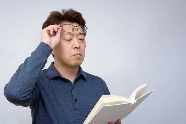 Asian male trying to read something in his book. poor sight, presbyopia, myopia.