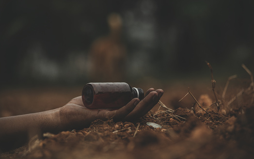 Concept of Farmer Suicide, closeup of hands with poison bottle at farm or agriculture land