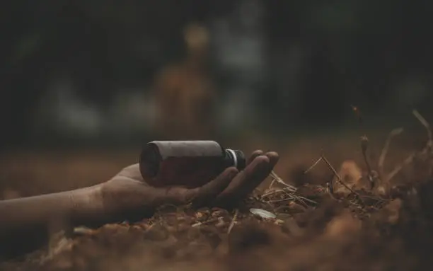 Photo of Concept of Farmer Suicide, closeup of hands with poison bottle at farm or agriculture land.