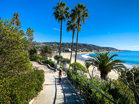 A young 9 year old girl walks her 6 month old Shih Tzu puppy along a path towards a beautiful sunny Laguna Beach during the quieter Autumn months.  Laguna Beach is a small coastal city in Orange County, California. It is known for a mild year-round climate, scenic coves, environmental preservation, and an artist community. Shot in November on an iPhone Xs Plus.