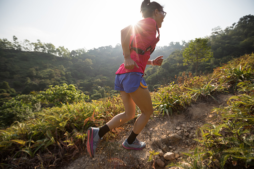 Woman trail runner running up on mountain slope in tropical forest