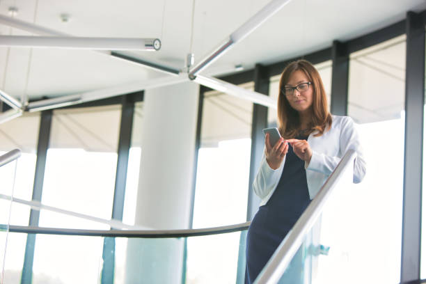 istock Low angle view of businesswoman using on smartphone while standing at office 1192037277