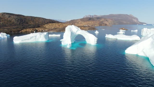 Slow and majestic drone aerial view over white and turquoise Icebergs floating in the calm Baffin Sea, Greenland