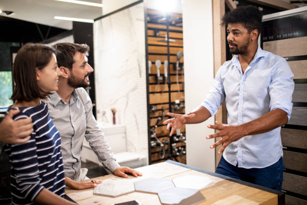 A store seller putting some ideas together on a couple of hexagonal tile samples on a table with a husband and wife in a bathroom equipment and accessories shop