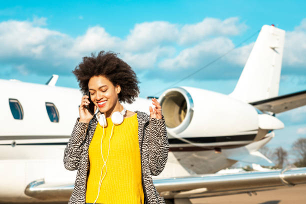 joven empresaria multiétnica hablando por un teléfono móvil cerca de un avión privado - status symbol audio fotografías e imágenes de stock