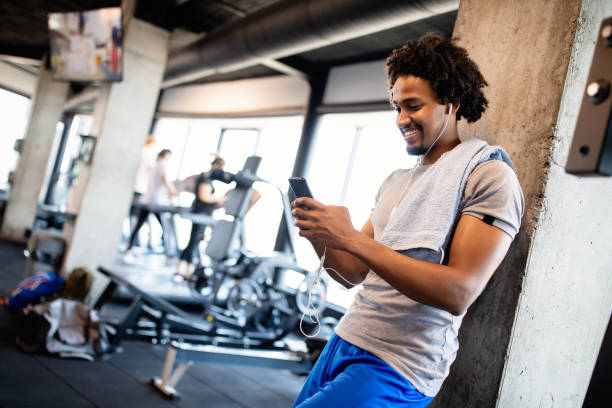 運動休憩中にジムで携帯電話を使用する若い筋肉の男 - health club social gathering exercising sport ストックフォトと画像