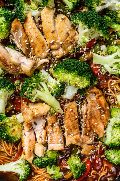 Asian egg noodles with vegetables and meat on cooking pan. Gray background. Top view