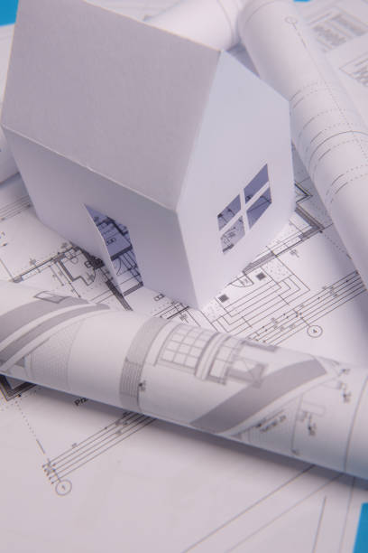 istock White family paper house, house projects plan and blueprints in the background. Minimalistic and simple concept, style. Horizontal orientation. View from above 1192064708
