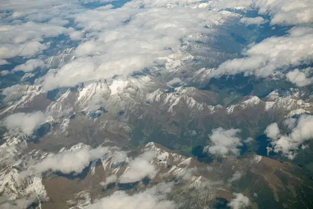 Photo of Aerial view of jaggy mountain peaks in the European Alps seen through the window of a commercial aircraft flying overhead.