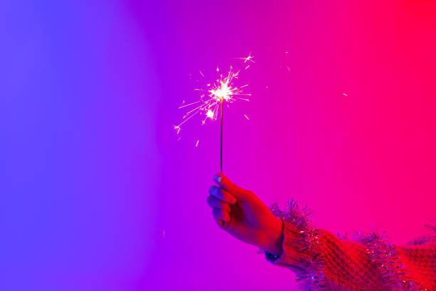 Concept of new year party or celebration: hand in sweater holding bengal fire against vivid neon lights