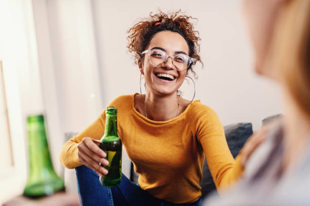 Young attractive smiling caucasian tanned woman with curly hair sitting with her best female friend, chatting and drinking beer. Young attractive smiling caucasian tanned woman with curly hair sitting with her best female friend, chatting and drinking beer. woman drinking beer stock pictures, royalty-free photos & images