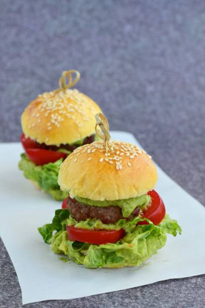 Sesame seed burger buns with beef patties, guacamole, tomato and lettuce