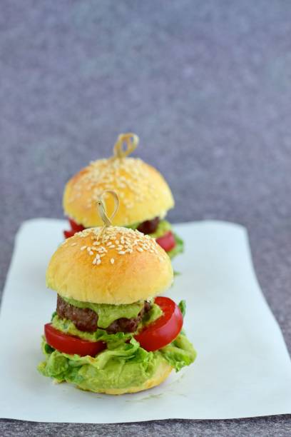 Sesame seed burger buns with beef patties, guacamole, tomato and lettuce