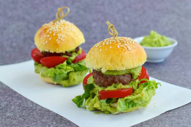 Sesame seed burger buns with beef patties, guacamole, tomato and lettuce
