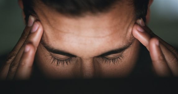 Closeup shot of a young businessman suffering with a headache while working in an office at night