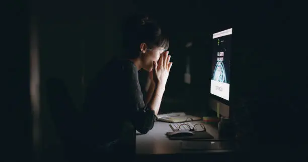 Shot of a young businesswoman looking stressed out while working on a computer in an office at night