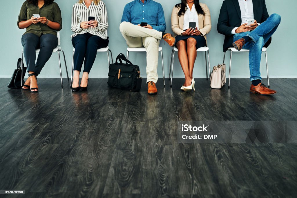 Tech savvy and ready to ace the interview Studio shot of a group of businesspeople using their smartphones while waiting in line against a blue background Adult Stock Photo