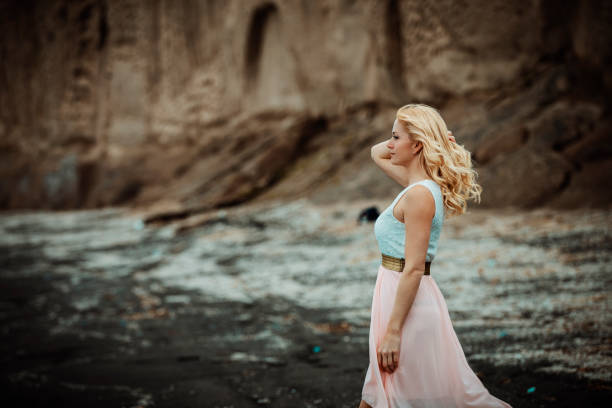 blond woman on a black sand beach on Santorini, with a cliff in the background and a rough sea