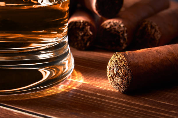 nature morte avec le verre de whiskey ou de rhum, cigare sur la vieille table en bois de conseil. fond flou. - cigar whisky bar cognac photos et images de collection