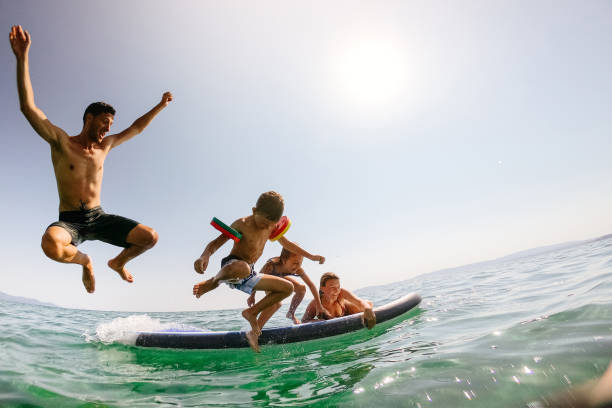 famiglia felice che salta in mare - surfing beach family father foto e immagini stock
