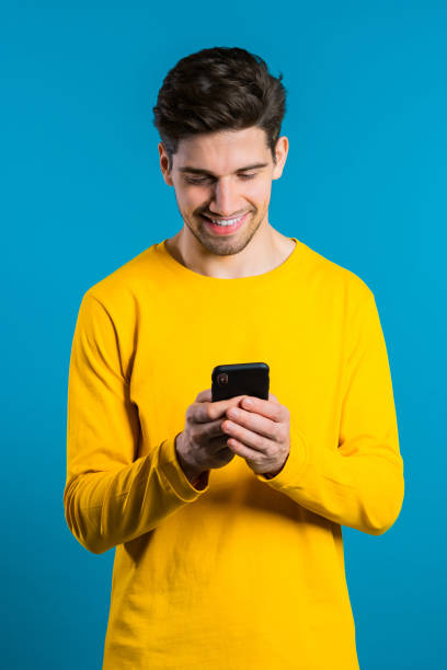 istock Man sms texting using app on smartphone. Handsome young guy surfing internet with mobile phone. Blue studio background 1192091327