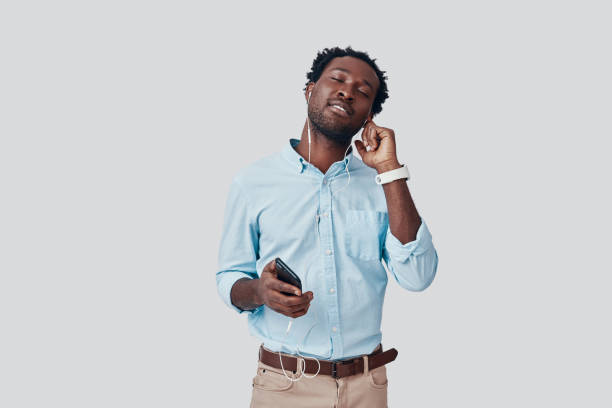 istock Handsome young African man listening music and smiling while standing against grey background 1192093471