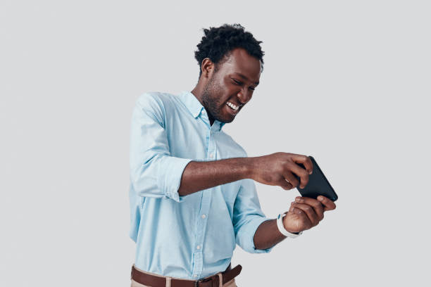 istock Handsome young African man playing mobile game and smiling while standing against grey background 1192094108
