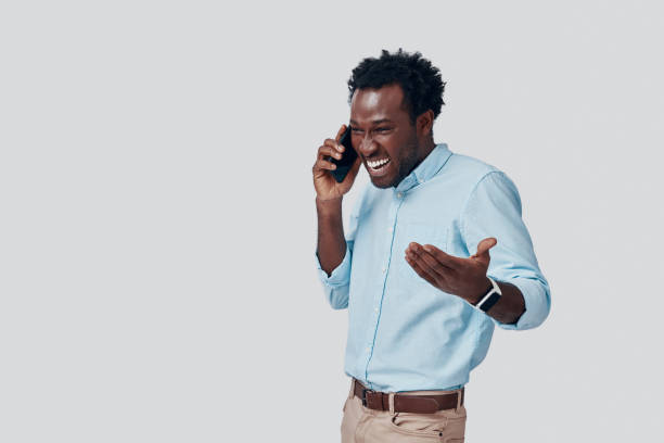 istock Handsome young African man talking on the phone and smiling while standing against grey background 1192094295