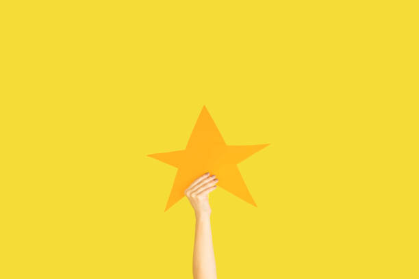 istock Hands holding the sign of star on yellow studio background 1192094496